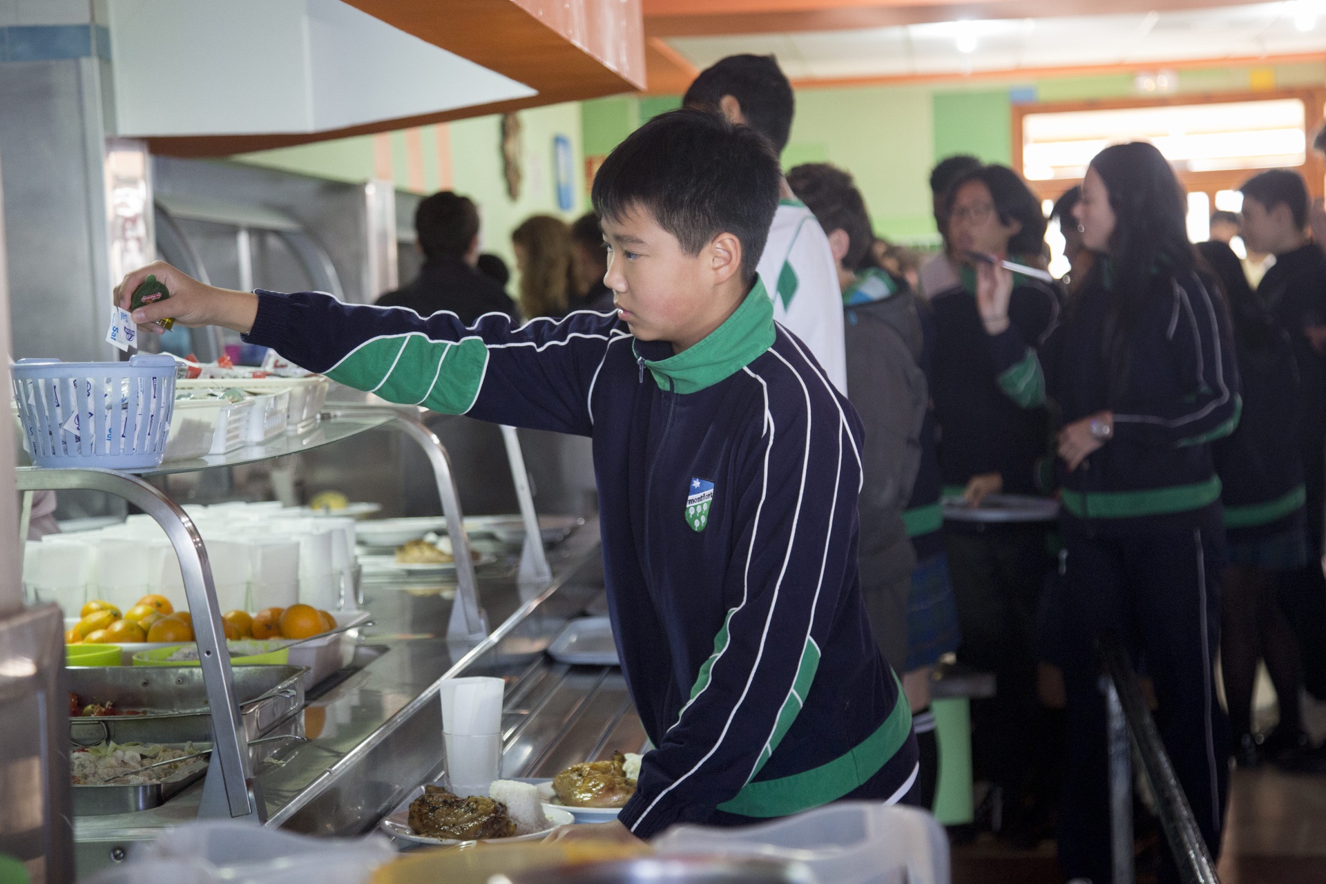 A group of students lined up in a cafeteria, with one student serving himself food.